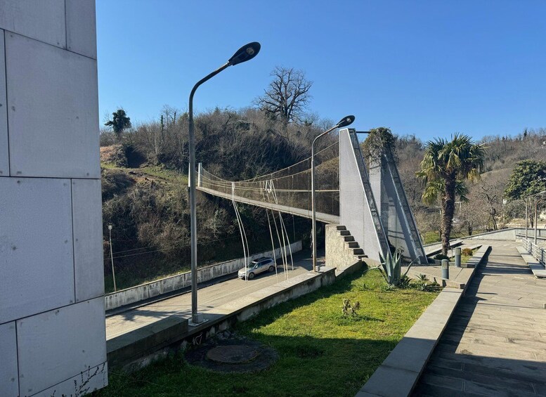 A pedestrian bridge with metal railings, a car on the road below, and a clear blue sky. 3