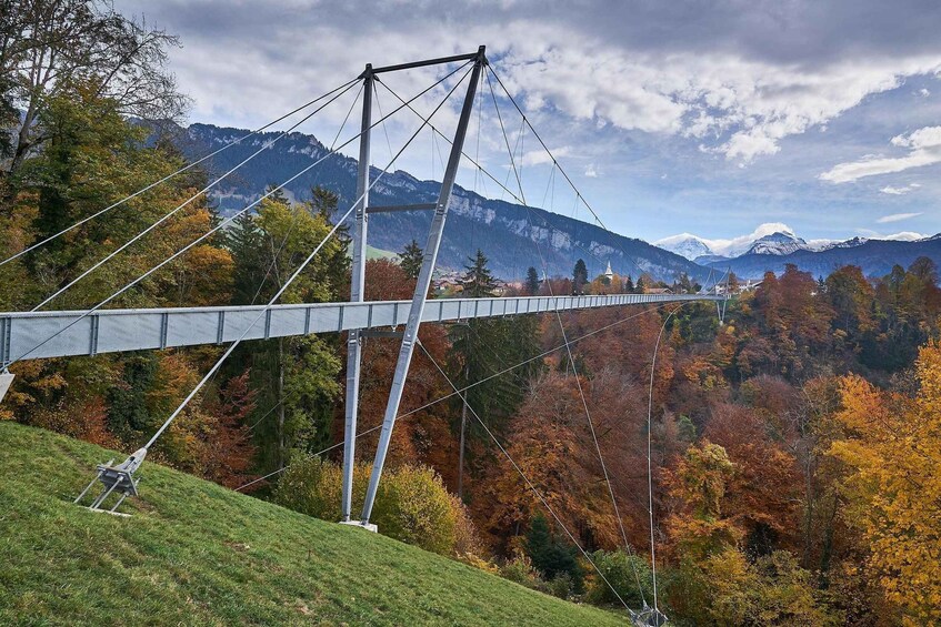 A suspension bridge over a forested valley with autumn foliage and snow-capped mountains in the background. 3