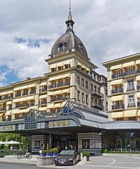 A grand hotel with a prominent dome and multiple balconies with yellow awnings. 1