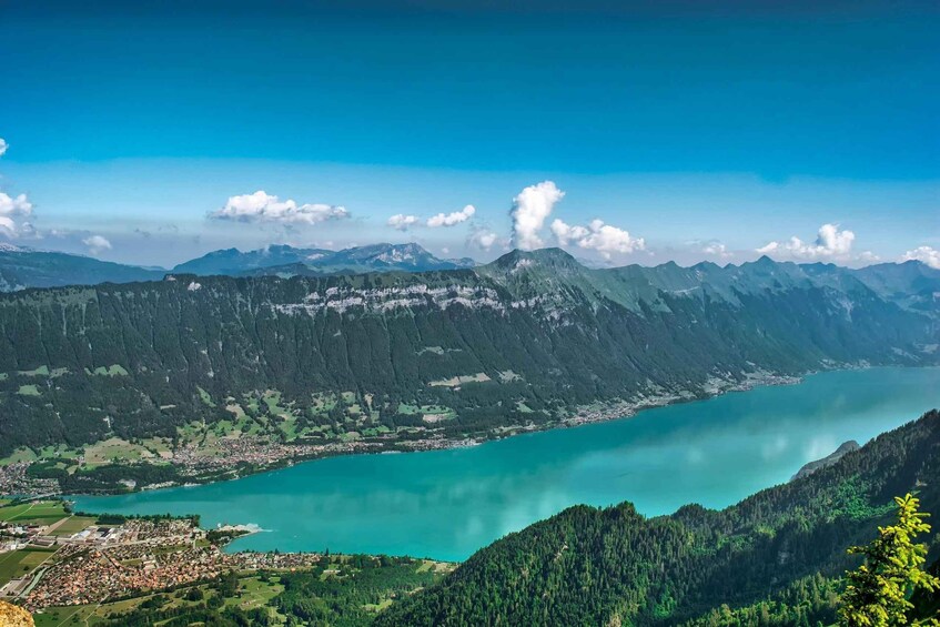 A mountainous landscape with a turquoise lake, a town in the valley, and a forested mountain range. 5