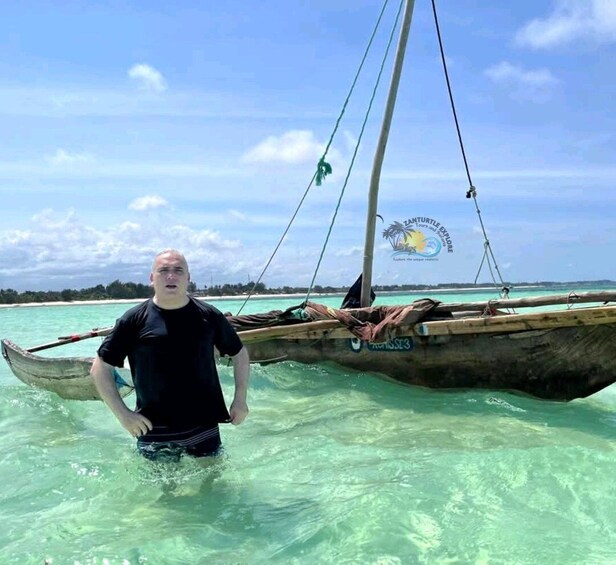 A person standing in shallow water next to a traditional boat. 4