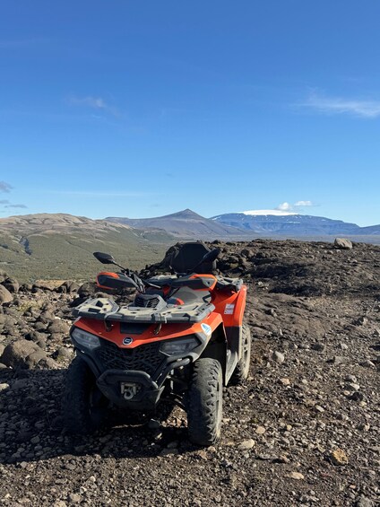 An orange ATV parked on rocky terrain with a mountainous landscape in the background. 3