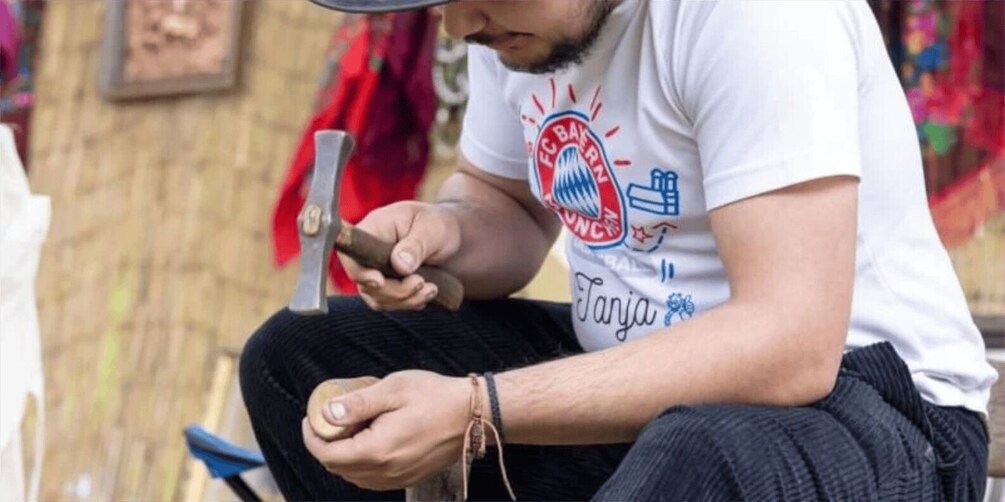 A person sitting on a bench, wearing a white t-shirt with a logo and text, holding a smartphone. 2