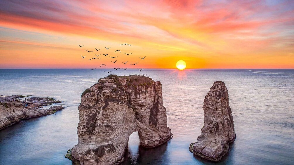 A sunset over a coastal landscape with rock formations and birds flying. 1