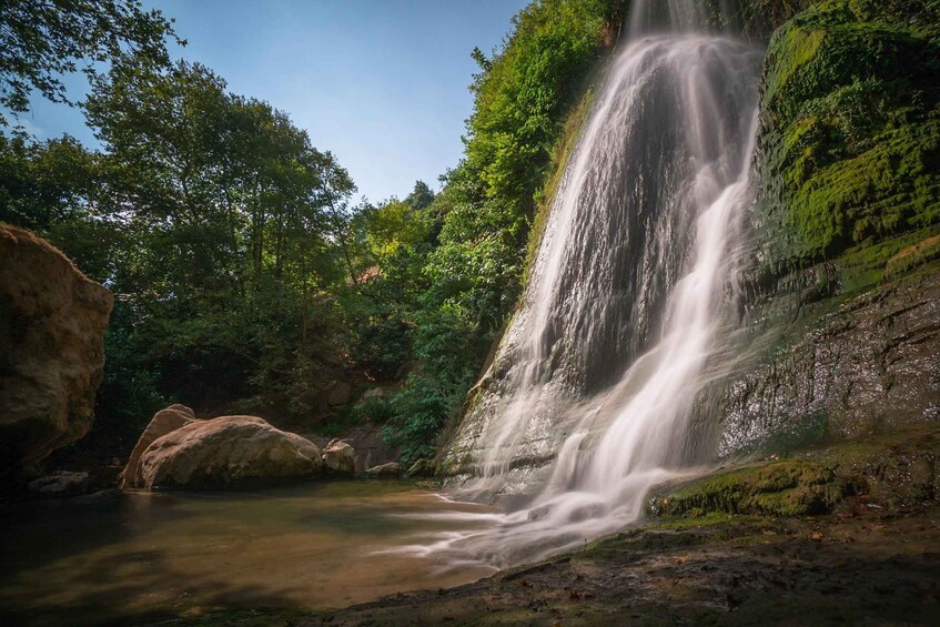 A waterfall cascading into a pool surrounded by lush greenery and large rocks. 5