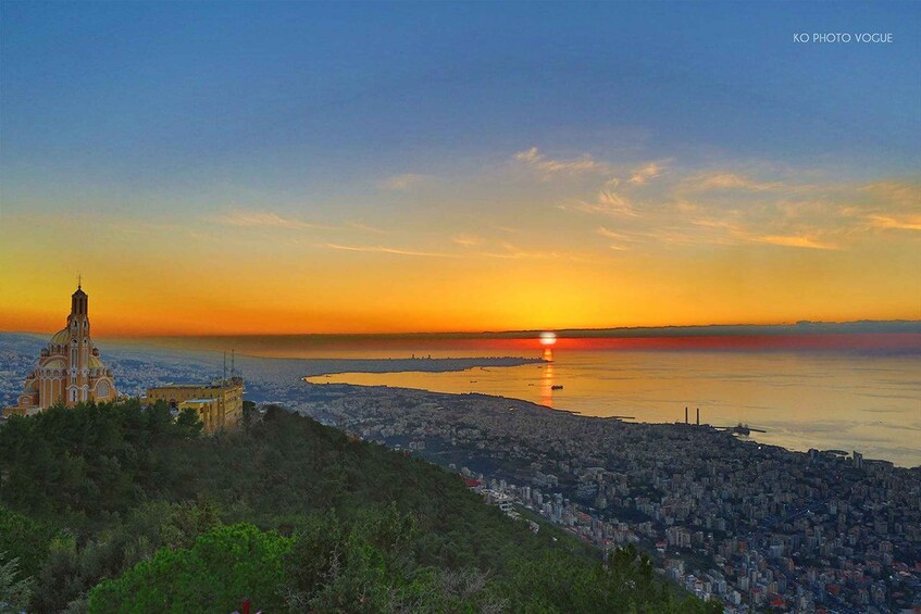 A cityscape at sunset with a prominent church on a hill, a body of water in the foreground, and a clear sky. 2