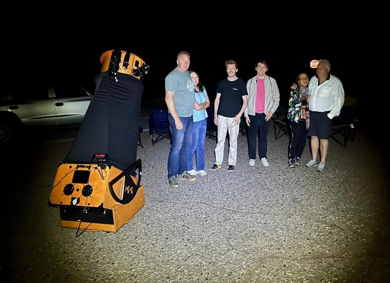 A group of people standing outdoors at night with a large, orange, vintage car in the foreground. 3