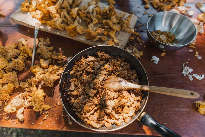 A wooden table with a pan of cooked chicken and vegetables, a wooden spoon, and a metal bowl. 5