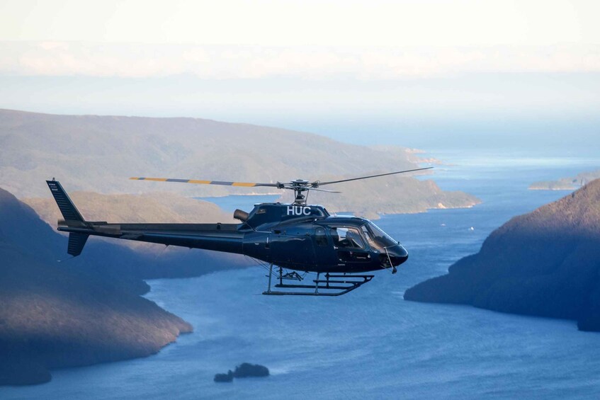 A helicopter with 'HUC' on its side flying over a coastal area with cliffs and water. 1
