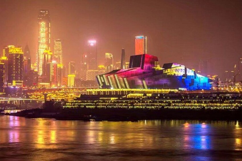 A brightly lit building with a unique architectural design, a city skyline with illuminated skyscrapers, and a body of water reflecting the lights. 4