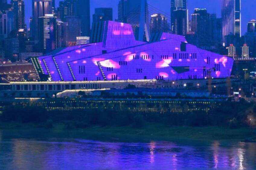 A city skyline with illuminated buildings and a large, uniquely shaped structure with purple lighting. 3