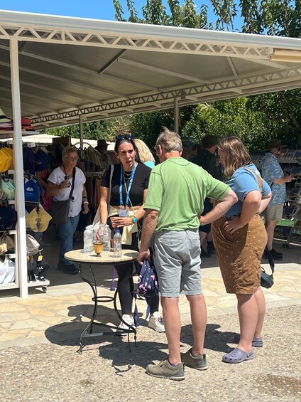 People at an outdoor market with a covered area, tables, and various items on display. 3