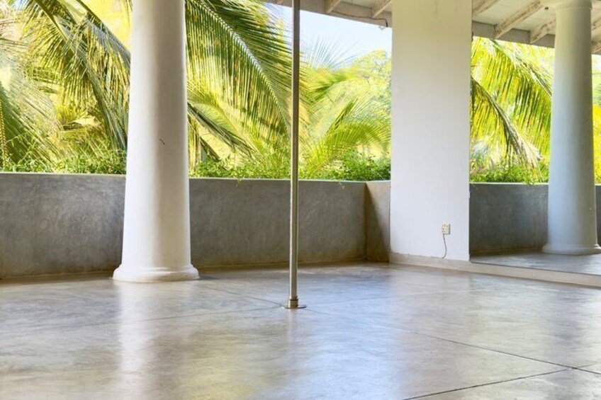 A covered outdoor area with a polished concrete floor, white columns, and a view of palm trees. 2