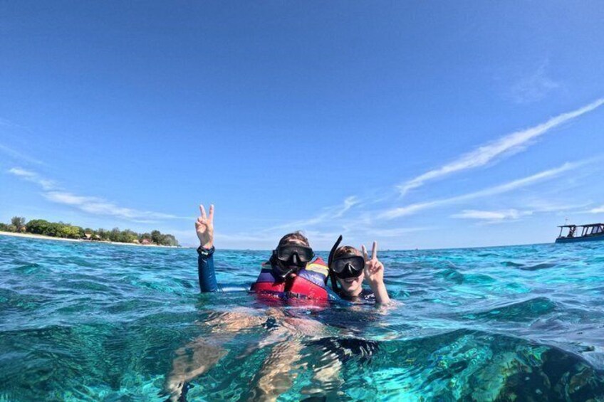 Two people snorkeling in clear blue water with a boat in the background. 4