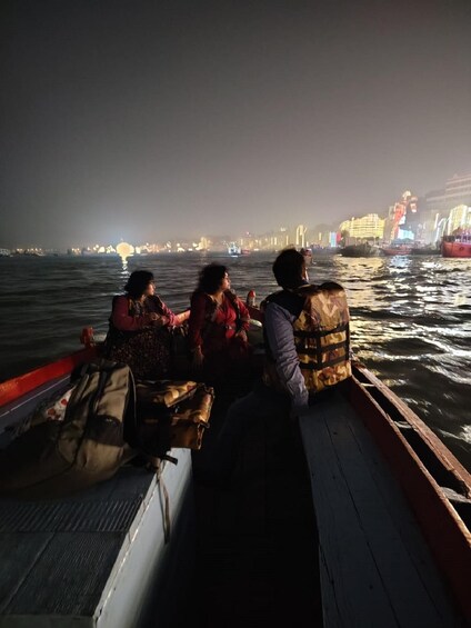 A nighttime boat ride with passengers wearing life jackets, a city skyline in the background, and illuminated buildings. 3