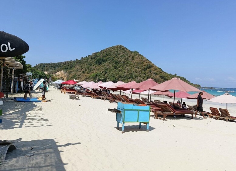 A beach with sun loungers and umbrellas, a mountain in the background, and a clear sky. 3