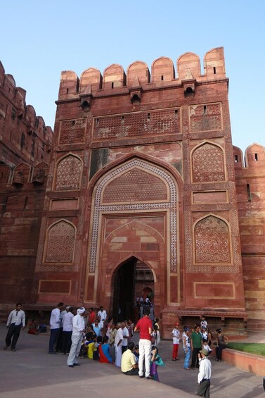 A large, ornate red-brick gate with intricate carvings and a central archway, surrounded by a crowd of people. 4