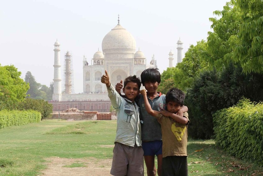 Three children standing in front of the Taj Mahal with one giving a thumbs-up. 3