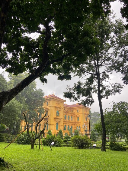 A historic yellow building with green windows, surrounded by lush greenery and trees. 2