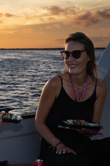 A person holding a tray of food on a boat with a sunset in the background. 4