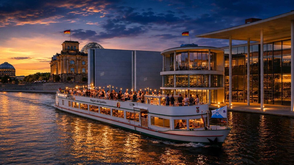 A boat with passengers, a modern building, and a historic structure with a dome by the river at sunset. 1