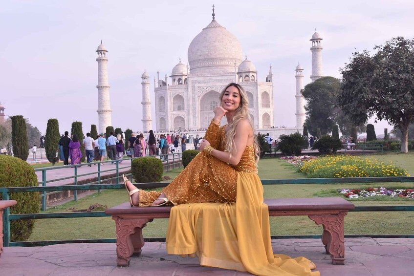 En kvinde i en gylden kjole sidder på en bænk foran Taj Mahal. 4