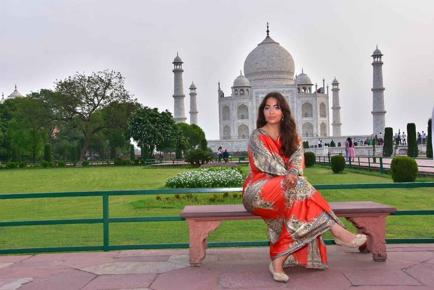 En person sidder på en bænk foran Taj Mahal, med monumentet og haverne i baggrunden. 2