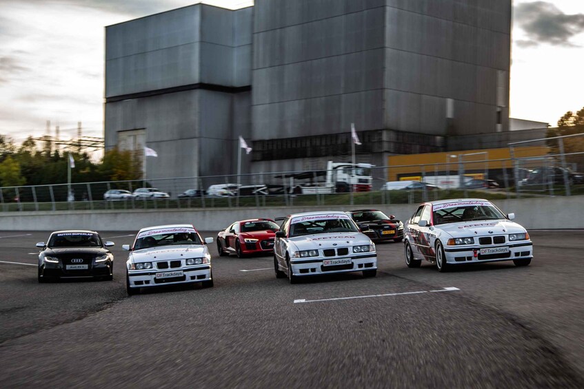 A group of racing cars on a track with a modern building in the background. 1