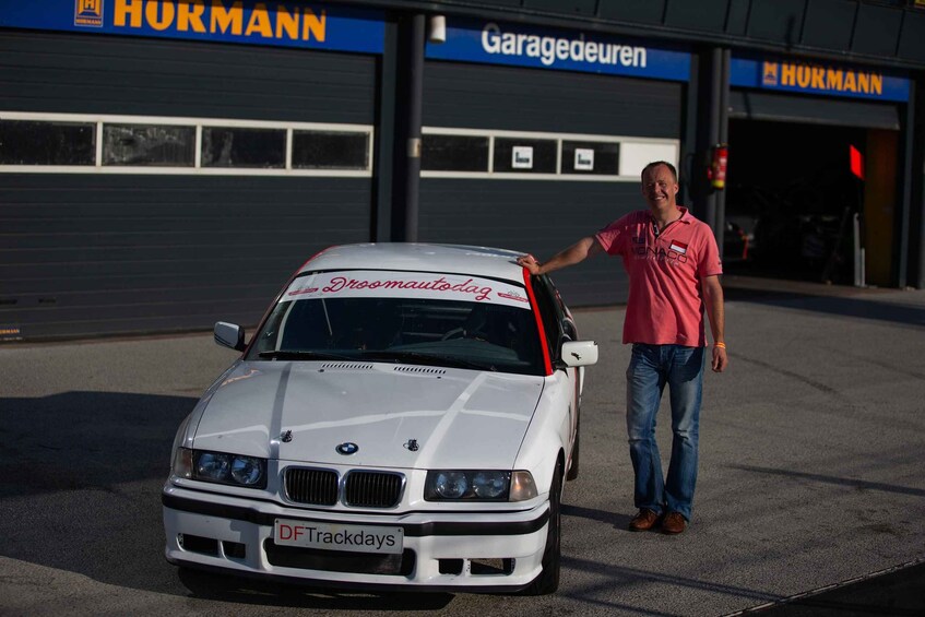 A white BMW with 'DFTrackdays' on the front, parked in front of a building with 'HURMANN' signage. 5