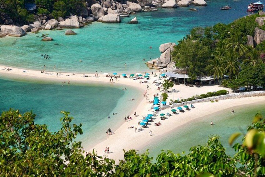 A beach with clear turquoise waters, large rocks, and palm trees. 1