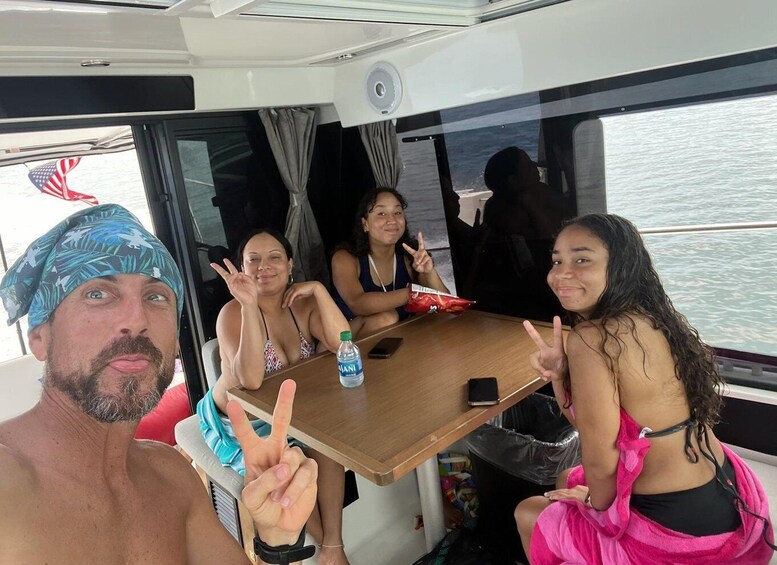A group of people on a boat with a table, a bottle of water, and a flag visible. 3