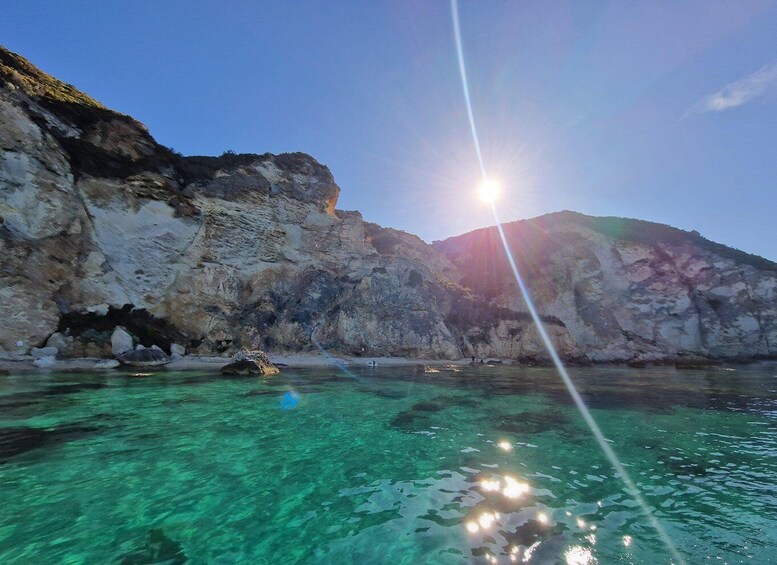 A coastal landscape with clear turquoise waters, rocky cliffs, and the sun shining through. 3
