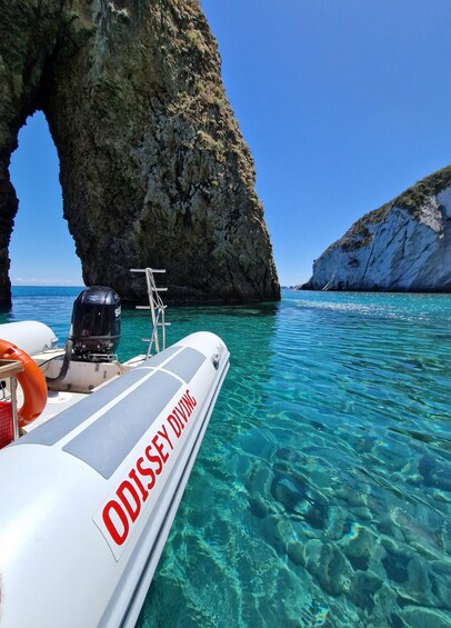 A boat named 'ODISSEY DIVING' anchored near a rocky coastline with clear turquoise water. 4