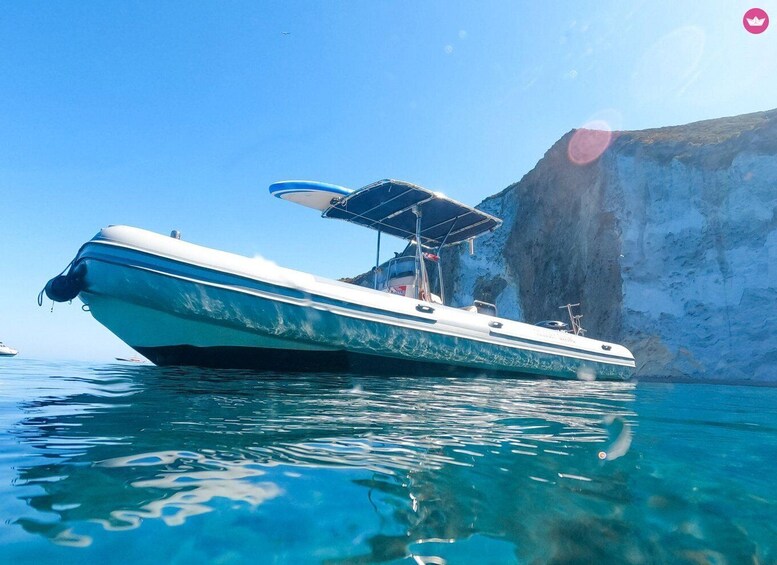 A boat with a canopy on a clear blue sea, with a rocky cliff in the background. 1