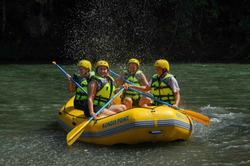 A group of people in a yellow inflatable raft with paddles, wearing helmets and life vests, on a river. 4