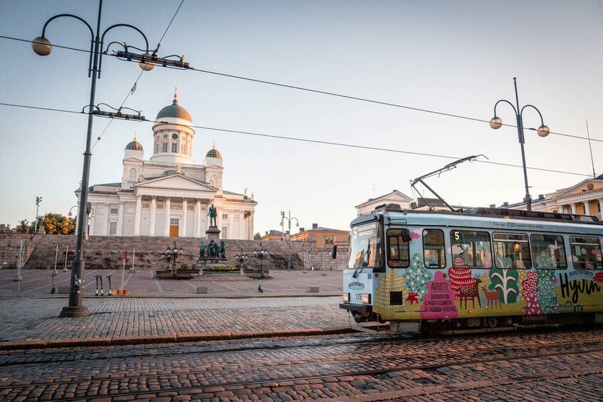 A tram with colorful artwork, a historic building with domes, and a cobblestone square. 3