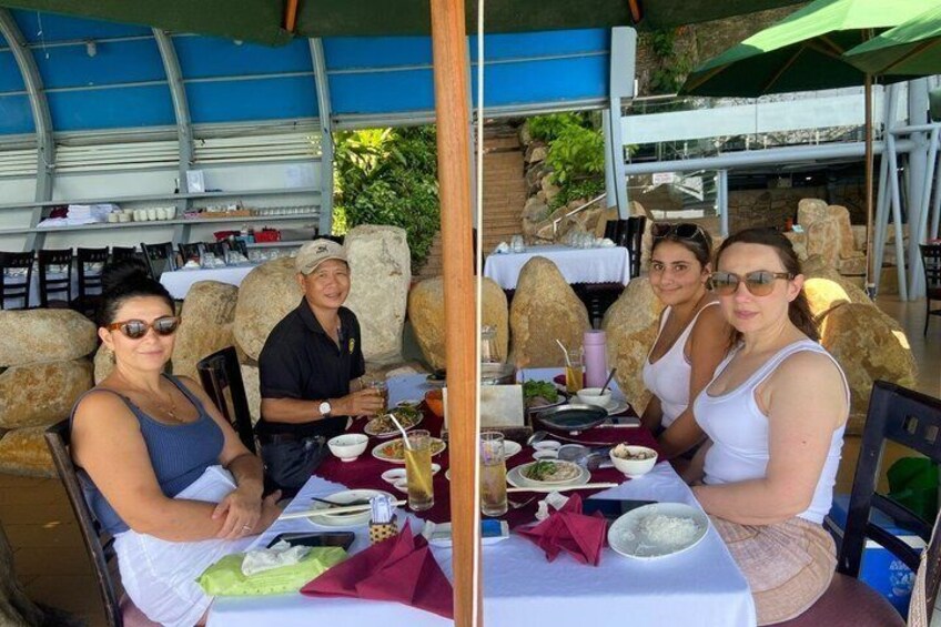 A group of people dining at an outdoor restaurant with stone seating and a blue canopy. 3