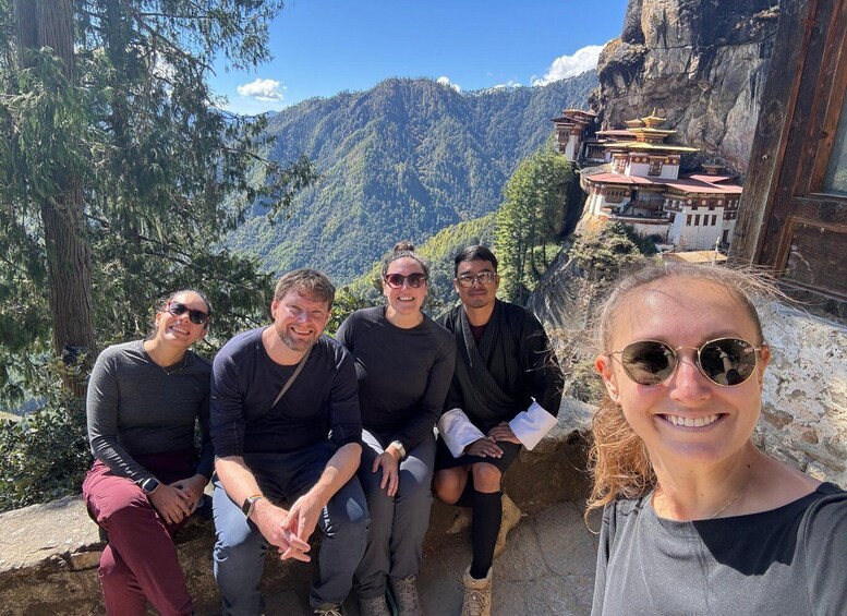 A group of people sitting on a ledge overlooking a mountainous landscape with traditional buildings. 3