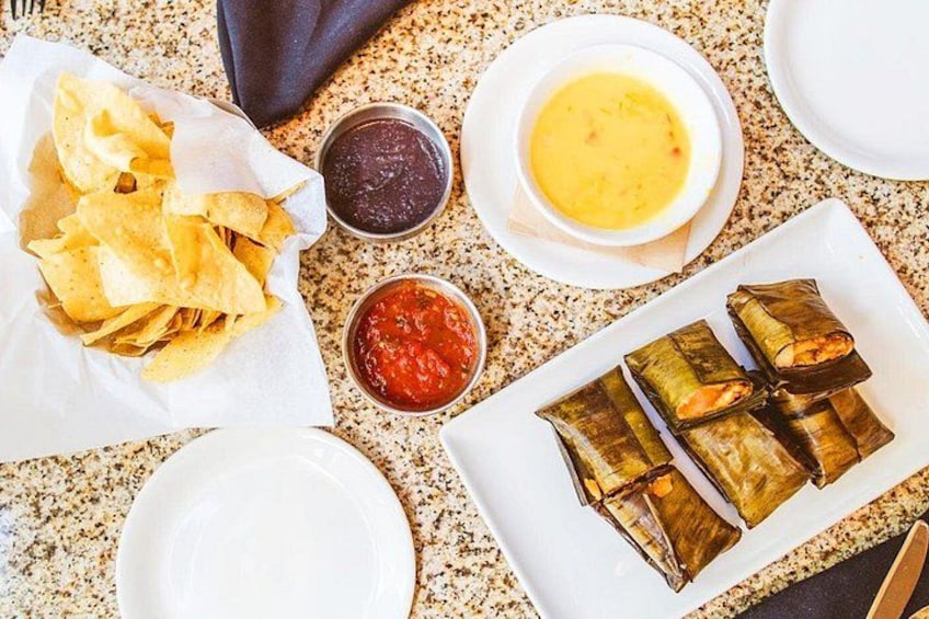 A table with food items including chips, tamales, and various sauces. 5