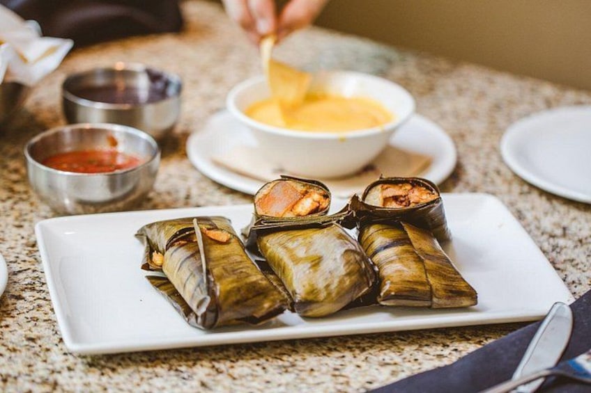 A plate of tamales with a dipping sauce and a bowl of sauce. 1