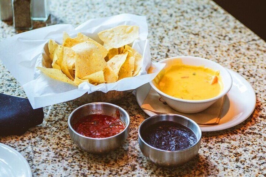Nachos, a bowl of soup, and two small containers of salsa. 5