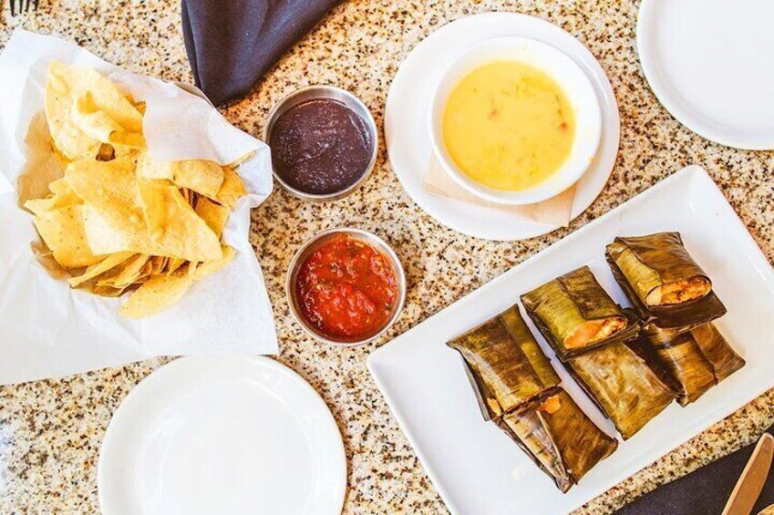 A table with food items including chips, a bowl of soup, and tamales. 4