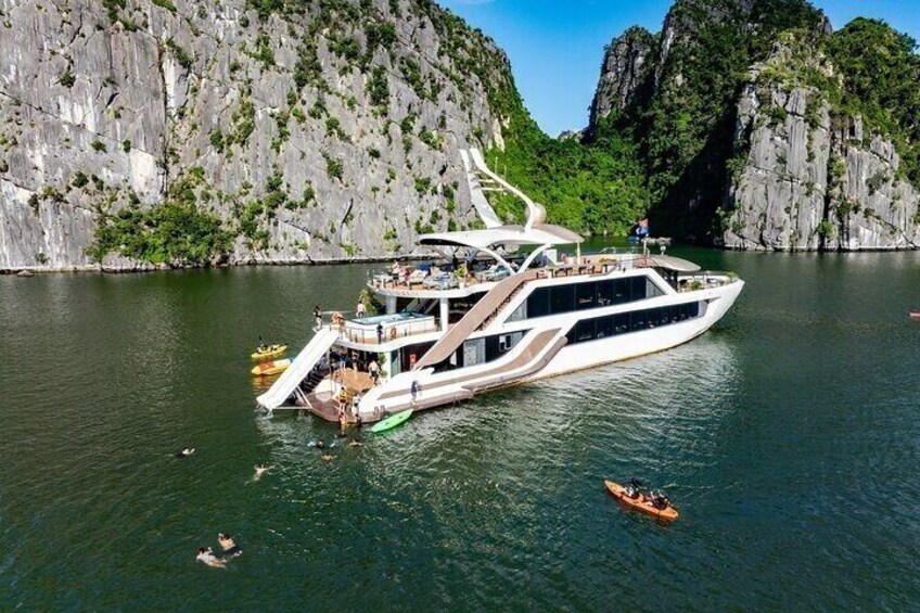 A large white yacht docked near rocky cliffs with a person in a kayak nearby. 1