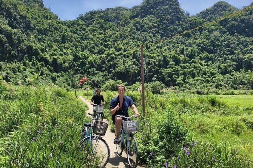 Two people riding bicycles on a dirt path surrounded by lush greenery and hills. 5