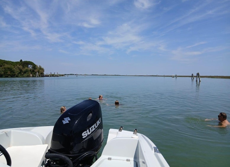 A boat with a Suzuki motor on the water, people swimming, and a distant shoreline with trees and structures. 1
