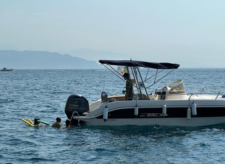 A boat with a Yamaha outboard motor on calm sea water, a person standing on the deck, and a distant shoreline with mountains. 5