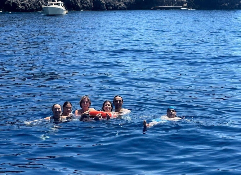 A group of people swimming in a body of water with a boat in the background. 2