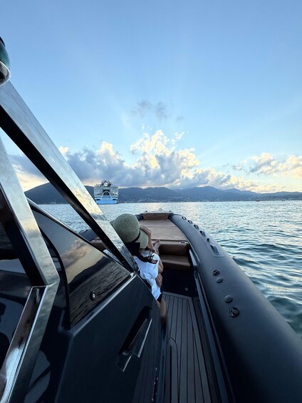 A boat with a person holding a hat, water, and distant mountains. 1