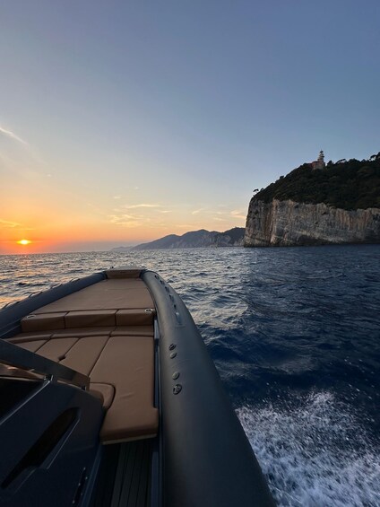 A boat on the water with a sunset in the background and a lighthouse on a cliff. 5