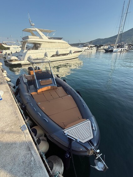 A small inflatable boat docked at a marina with larger yachts in the background. 3